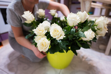 Woman puts white roses in a green pot.