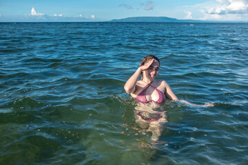 A sexy asian woman in a bikini wading in chest deep waters during a sunny day at the beach....