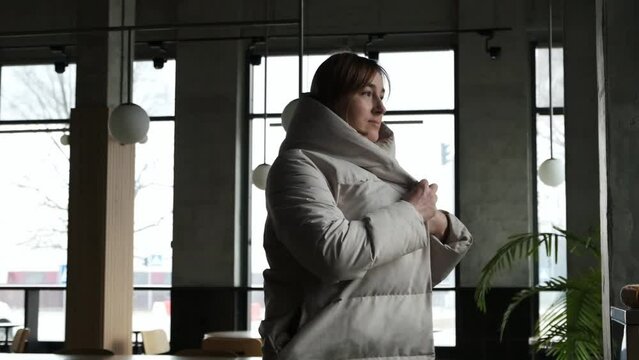 Young caucasian woman putting on big warm white down jacket in a slow motion. Getting warm during cold winter days