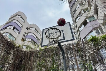 Basketball screen and rim with a ball bouncing off on a court between blocks of flats.