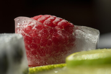 alcuni cubetti di ghiaccio con al loro interno laponi e mirtilli, con fette di lime, un piano in ardesia con al di sopra dei cubetti di ghiaccio con frutta