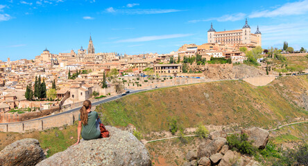 woman tourist sitting on rock looking at panorama view of Toledo city landscape in Spain - obrazy, fototapety, plakaty