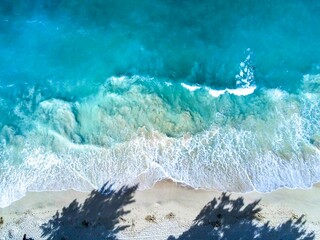 Aerial top view of the waves crashing on the beach with a shadow of trees in Waimanalo, Oahu, Hawaii