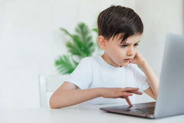 a child sits with a laptop at a table in a room with a green plant