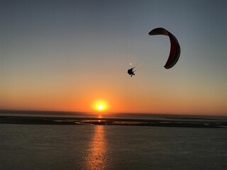 Silhouette shot of a paraglider landing on a land surrounded by water with sunset in the background