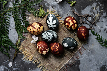 Easter eggs dyed with natural ingredients like cabbage, onion peel, hibiscus tea carcade with beatiful patern on rustic wooden tray and craft paper.
