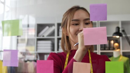Creative businesswoman using post-it notes on glass wall to write strategic business plan to develop success, businesswoman sticking post-it on glass