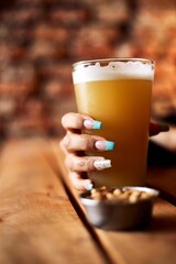 Vertical shot of a woman with painted nails holding a pint of beer at a pub