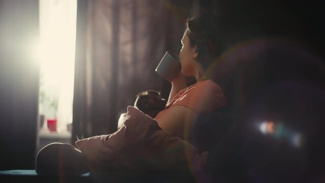 A Caucasian woman holds a dog in her arms and drinks morning coffee. Happy girl with pet. The concept of love for animals, happiness. High quality 4k footage