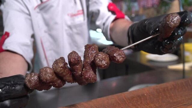 Chef placing cevapcici on an iron spear in preparation for meal service.