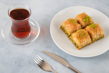 Pistachio baklava on a white plate with Turkish tea.A plate of traditional baklava on light blue background
