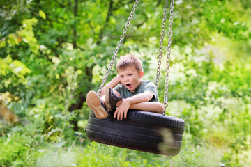 sad and boring boy yawning in a swing tire in the forest. Quarrel with friends, resentment, loneliness, boredom, yearning