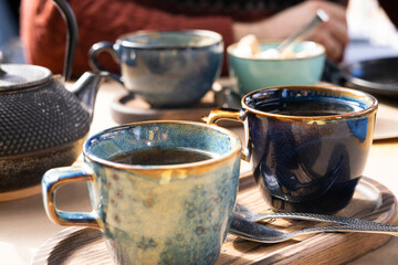 Brewing and Serving Tea. Teapot Poured Green Tea Blue Ceramic Cup on Wooden Cafe Table. Two Pottery...