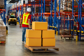 warehouse worker pulling packages on pallet moving cart between tall shelves in warehouse factory. Wholesale Merchandise. shelves, pallets and boxes