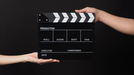 Two hands send and hold Black clapper board or movie slate on black background.