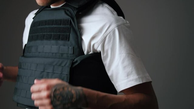 Unrecognisable young adult man wearing black bulletproof jacket on his torso. Gray background. Studio shot. High quality 4k footage