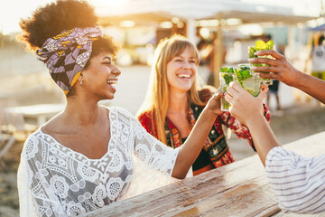 Multiracial happy friends cheering and drinking mojitos at beach party - Focus on right hand...