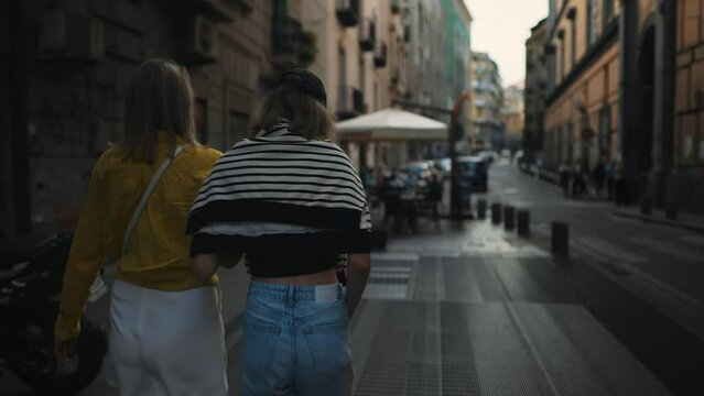 Two women are walking around the summer city. Back view.