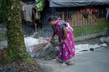 South asian rural housewife sweeping house yard with a broom wearing traditional clothes named as saree