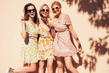 Three young beautiful smiling hipster female in trendy summer dresses clothes. Sexy carefree women posing in the street. Positive models having fun, talking, chatting, communicating. Going crazy