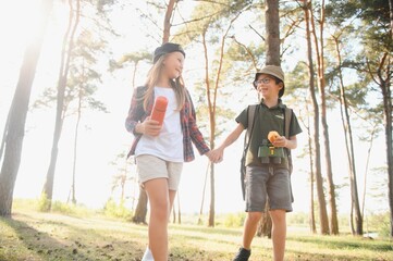 Obraz premium Happy excited school children with backpacks in casual clothes enjoying walk in forest on sunny autumn day, two active kids boy and girl running and playing together during camping trip in nature.