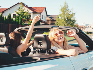 Portrait of two young beautiful and smiling hipster female in convertible car. Sexy carefree women...