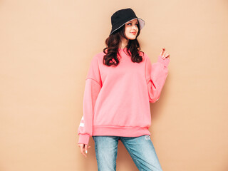 Young beautiful smiling female in trendy summer jeans and pink sweater clothes. Sexy carefree woman posing near beige wall in studio. Positive model. Cheerful and happy. In panama