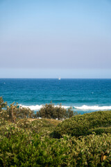 Beautiful romantic view of the white sailboat in the ocean visible from the path on the hill leading to the beach.  