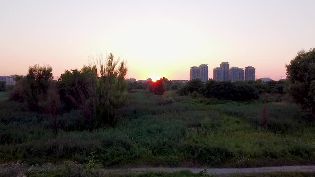 Stunning Sunset Aerial Footage- Vacaresti Delta's Breathtaking Beauty with Lush Greenery and Clear Skies, Featuring Romania's Majestic Tall Buildings in the Background