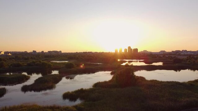 Aerial View At Sunset Of the Beautiful Vacaresti Delta With Lush Green Vegetation, Clear Sky And Tall Buildings In The Background, Romania