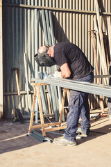 Man at work welding an iron bar with face protection