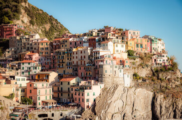 Fototapeta premium Manarola, a coastal town in Italy, showcasing the colorful houses that line the steep hillsides overlooking the sea, with a small harbor and boats in the foreground, and the blue waters 
