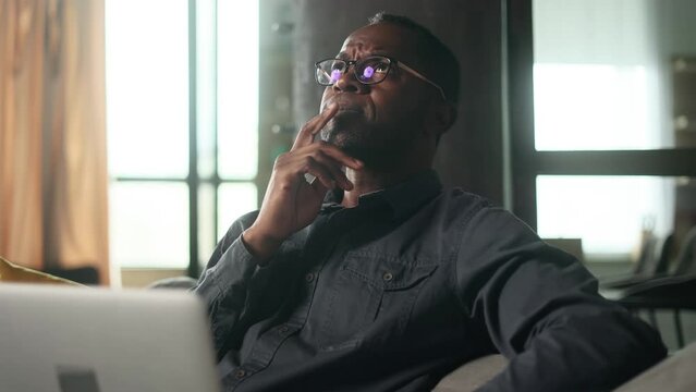 Portrait of mature african american man in eyeglasses thinks questioningly about difficult choice choose something imagine plan in mind has doubts create idea sitting on sofa at home