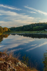 A picturesque reflection of the sky and trees in a forest river. The concept of vacation, summer, fishing, rest on the river bank, calendar, cover. Vertical photo. Blue sky, green trees.