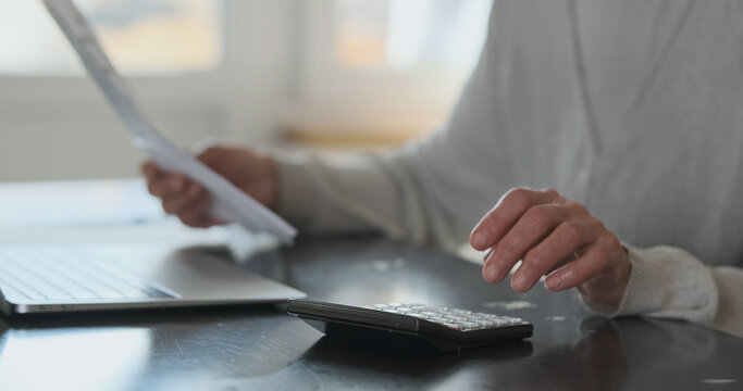 Elderly Woman's hands hold bills for services and calculate cost figures on calculator. Close-up, side view. Concept of financial literacy