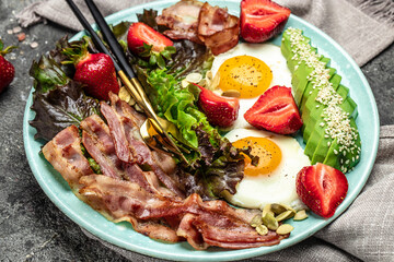 Plate with a keto diet food. fried egg, bacon, avocado, strawberries and fresh salad. Keto...
