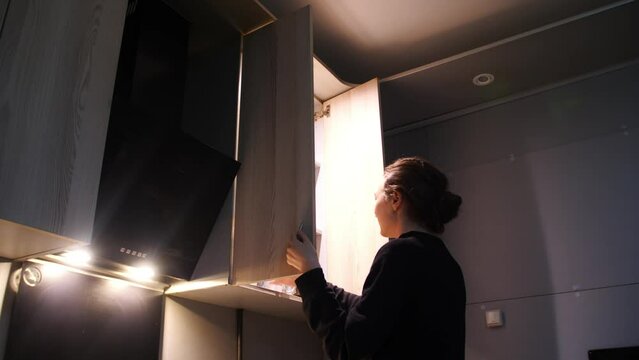 Woman open kitchenware drying rack with plates and cups in kitchen cabinet