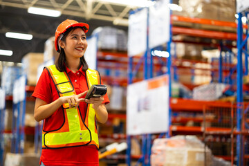 Warehouse female staff worker wearing hardhat helmet working on barcode scanner handheld at warehouse factory