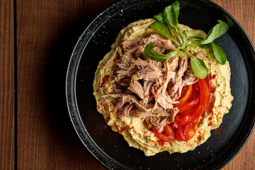 Hummus with chicken and pita in a black plate. Wooden background
