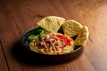 Hummus with chicken and pita in a black plate. Wooden background
