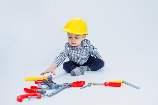 A little boy in a checkered shirt in the image of a builder. A boy in a construction helmet and plastic tools