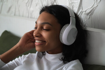 Side view portrait of happy african woman lying in bed with headphones on listening to music