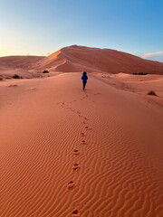 Fototapeta na wymiar Dunes in the Sahara desert, Merzouga desert, grains of sand forming small waves on the dunes, panoramic view. Setting sun. Morocco. Girl that walk on a sand dune. Shoe prints
