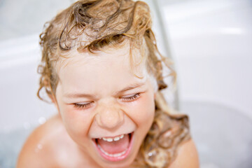 Cute child with shampoo foam and bubbles on hair taking bath. Portrait of happy smiling preschool girl health care and hygiene concept. Washes hair by herself.