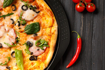 Pizza on a black dish on a dark wooden background.