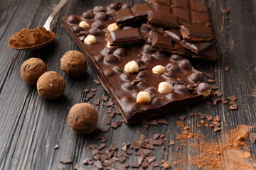 Handmade chocolate, cocoa powder in a spoon and chocolate truffles on a dark wooden background.