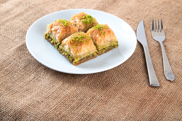 Traditional pistachio baklava in white plate.A plate baklava on burlap sack
