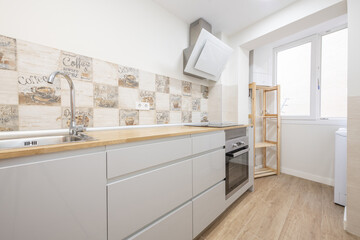 Kitchen furnished with smooth gray furniture without handles and wooden countertop and stoneware tiles