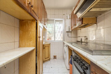 A very used and weathered apartment kitchen with very dilapidated wooden cabinets and an aluminum window in the background