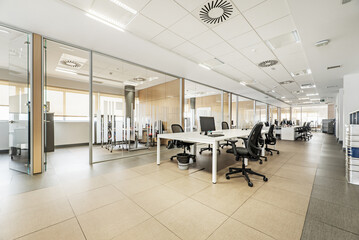 Professional office with large televisions and computer screens, glass panels to separate offices, technical ceilings, wooden meeting tables and identical swivel chairs